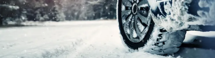 Un pneu de voiture enneigé est visible sur une route couverte de neige, avec des arbres en arrière-plan.