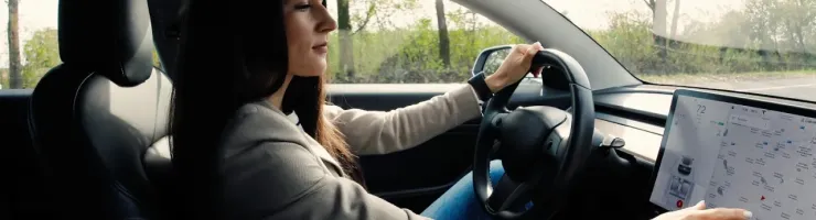 Une jeune femme aux cheveux longs conduit une voiture connectée, son regard tourné vers le tableau de bord numérique.