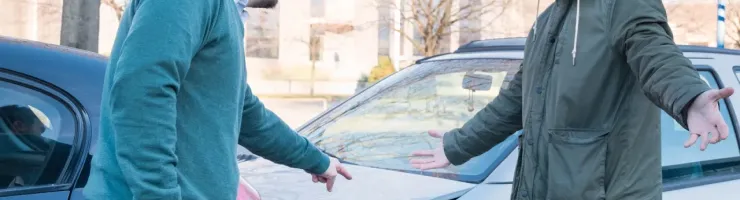 Deux hommes discutent avec des gestes expressifs devant les capots endommagés de leurs voitures après un accident.