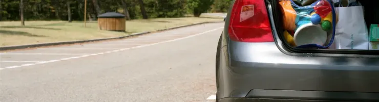 Le coffre ouvert d'une voiture grise révèle des sacs et des objets, garée sur un parking ensoleillé.