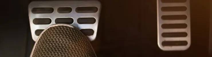 Un pied portant une chaussure grise est posé sur la pédale de frein d'une voiture, à côté de l'accélérateur.
