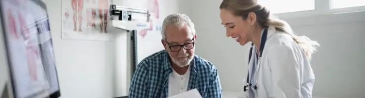 Un médecin souriant et un homme âgé examinent des documents dans un bureau médical.