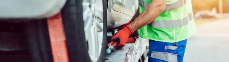 Un homme en gilet de sécurité fluo et gants rouges attache une voiture sur une dépanneuse.