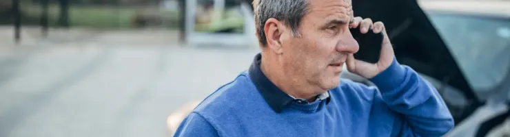 Un homme appelle au téléphone devant le capot ouvert d'une voiture en panne.