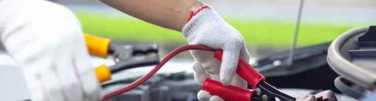 Des mains gantées raccordent des câbles de démarrage à la batterie d'une voiture.