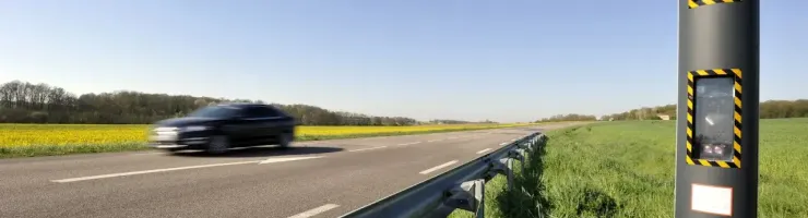 Un radar fixe est installé sur le bord d'une route de campagne, avec une voiture en mouvement rapide.