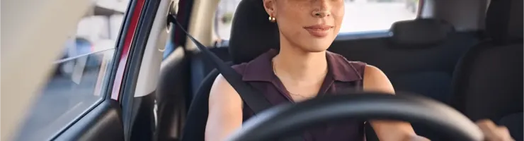 Jeune femme souriante et concentrée conduisant une voiture, ceinturée.