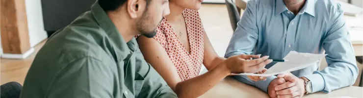Trois personnes autour d'une table, discutant de documents, probablement lors d'une réunion professionnelle.