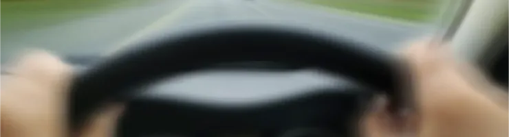Des mains tenant un volant, vue floue d'une route en mouvement.