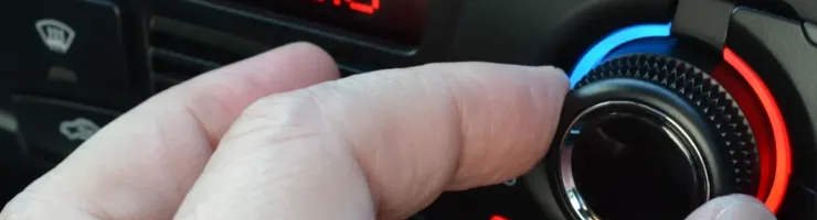 Gros plan d'une main ajustant un cadran de climatisation automobile affichant 20.0°C en rouge.