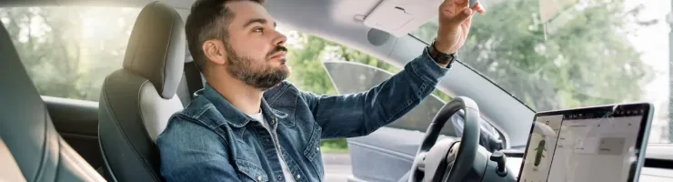 Un homme assis au volant d'une voiture moderne regarde dans son rétroviseur intérieur.