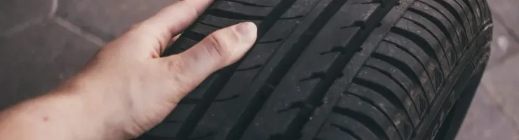 Une main touche la bande de roulement d'un pneu de voiture, inspectant l'état des sculptures sur le sol.