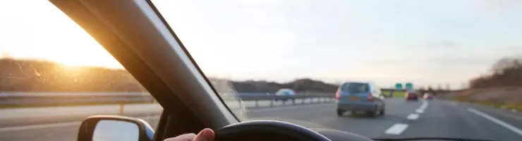 Vue du conducteur sur une autoroute au coucher du soleil, montrant les mains sur le volant et d'autres voitures en arrière-plan.