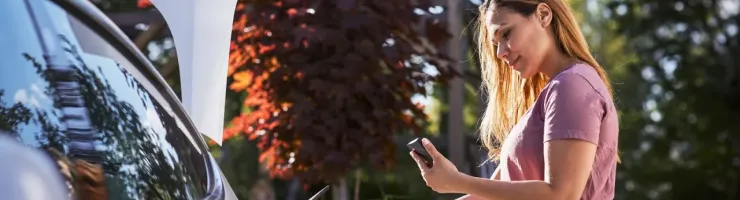 Une femme branche sa voiture électrique et regarde son téléphone.