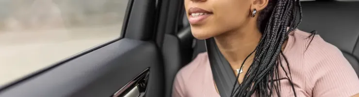 Une jeune femme assise à l'arrière d'une voiture, regardant par la fenêtre son téléphone dans les mains.