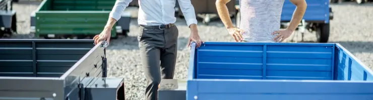 Deux hommes souriants et décontractés examinent des remorques de différentes couleurs dans un espace de vente extérieur.