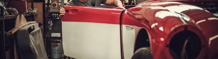 Un jeune mécanicien s'affaire sur une voiture de collection rouge et blanche dans un garage, la portière ouverte.