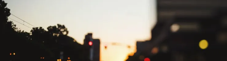 Vue floue de feux arrière de voitures dans la circulation urbaine au crépuscule, avec un ciel clair à l'horizon.