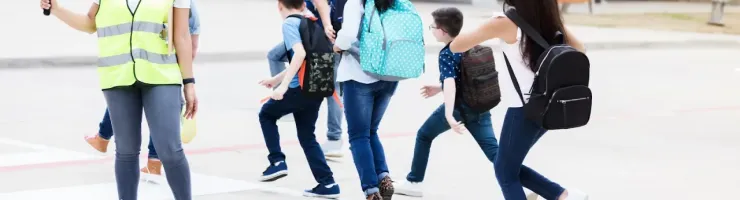 Une dame avec un panneau stop aide des enfants à traverser la route sur le passage piéton pour aller à l'école.