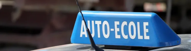 Gros plan d'un panneau bleu "AUTO-ECOLE" sur le toit d'une voiture, indiquant un véhicule d'auto-école.