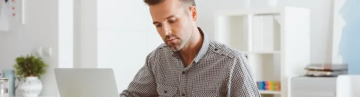 Un homme concentré travaille sur un ordinateur portable, tenant des documents dans un bureau lumineux et épuré.