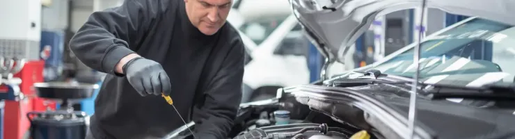 Un mécanicien expérimenté en gants noirs vérifie le moteur d'une voiture dans un garage, penché sur le capot ouvert.