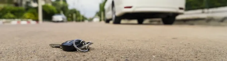 Des clés de voiture noires sont tombées sur la route, avec une voiture blanche garée en arrière-plan.