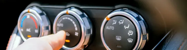 Une main est en train de régler les commandes de climatisation d'une voiture, visibles sur le tableau de bord.