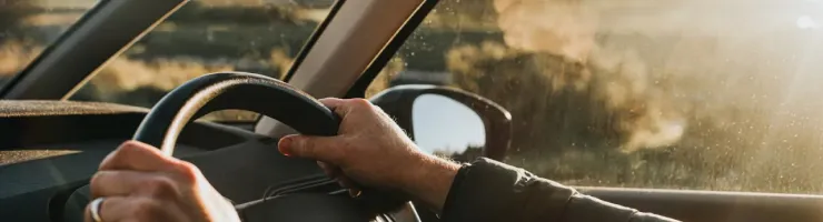 Vue de l'intérieur d'une voiture, montrant les mains d'une personne tenant le volant en conduisant au coucher du soleil.