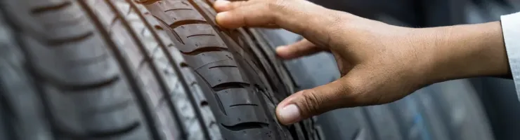 Une main touche un pneu neuf, montrant les sculptures de la bande de roulement.