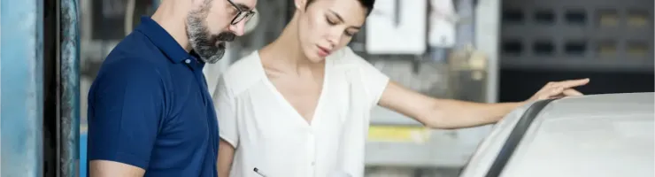 Un mécanicien et une femme regardent des documents près d'une voiture dans un garage.