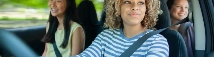 Une femme souriante au volant, avec deux passagères en arrière-plan, lors d'un trajet en covoiturage.