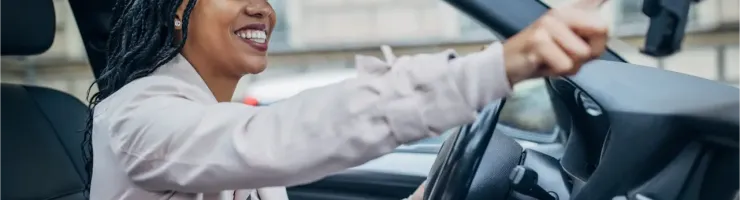 Une femme souriante aux tresses conduit une voiture et utilise son smartphone.