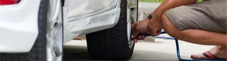 Une personne accroupie vérifie la pression et gonfle un pneu de voiture blanc.