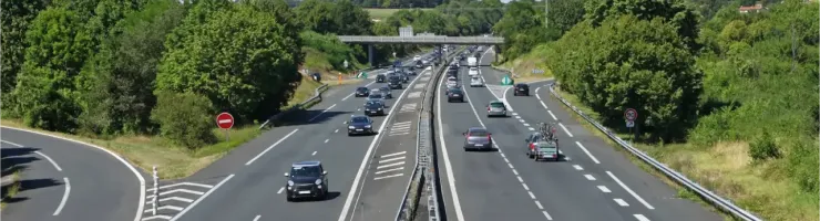 Vue aérienne d'une autoroute française avec plusieurs voitures en mouvement et un pont en arrière-plan.