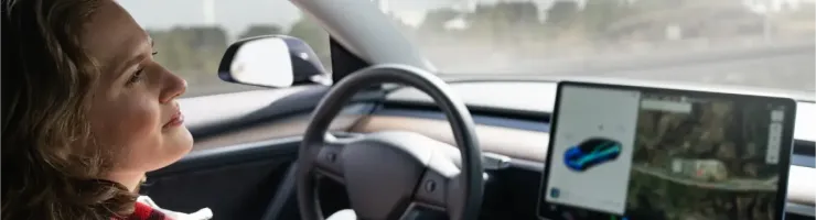 Une jeune femme souriante est assise au volant d'une voiture moderne, regardant le grand écran du tableau de bord.