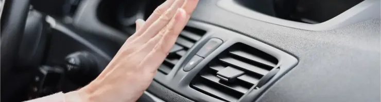 Une main est placée devant la bouche d'aération d'une voiture, vérifiant le flux d'air de la climatisation.