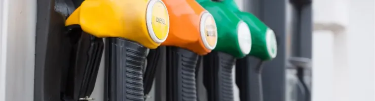 Gros plan sur plusieurs pistolets de différentes couleurs (jaune, orange, vert) à une pompe à essence.