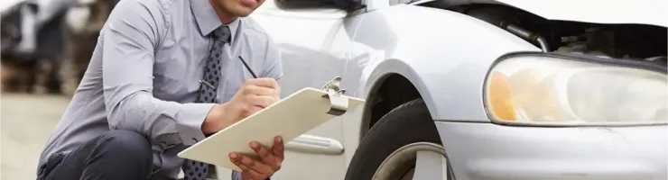 Un expert en sinistres examine une voiture endommagée et prend des notes sur un presse-papiers.