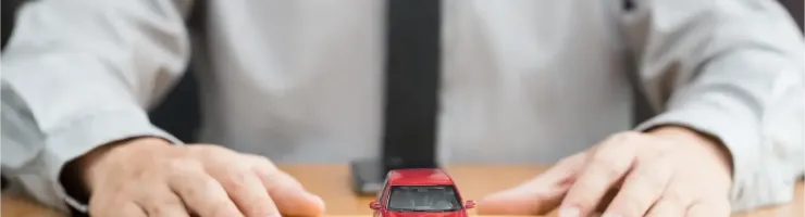 Les mains d'une personne derrière un petit modèle de voiture rouge posé sur une enveloppe marron.
