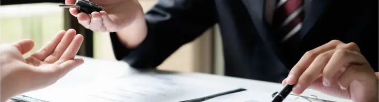 Une personne tend des clés de voiture à une autre personne au-dessus de documents sur une table.