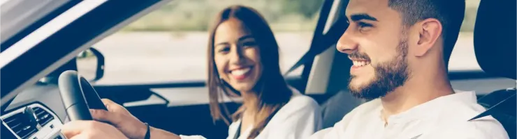 Un homme et une femme souriants à l'intérieur d'une voiture, l'homme au volant.