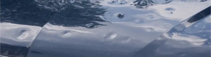 Capot de voiture bleu foncé avec de nombreuses bosses causées par la grêle.