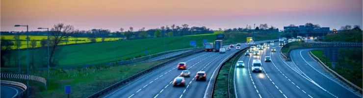 Autoroute très fréquentée au coucher du soleil avec des champs verts à l'arrière-plan.
