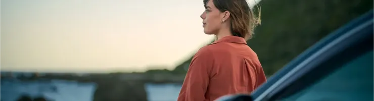Une femme regardant l'océan à côté de sa voiture.
