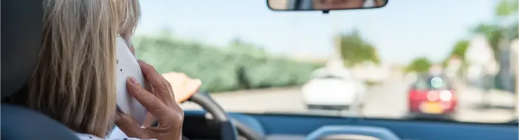 Une femme conduit une voiture tout en parlant au téléphone, vue de l'arrière.