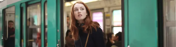 Une jeune femme aux cheveux roux regarde par la porte ouverte d'un metro à l'arrêt.