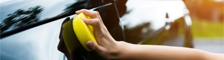 Une main tenant une éponge jaune lave la carrosserie noire brillante d'une voiture.