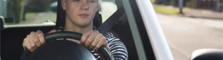 Un adolescent conduit une voiture sans permis, regardant dans son rétroviseur avec une expression concentrée.