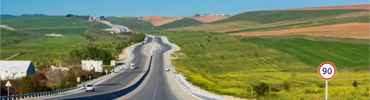 Longue route avec des collines verdoyantes et un panneau de limitation à 90 km/h.